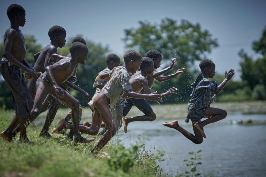 Group of children joyfully running and jumping near a river in Zaria, Nigeria.