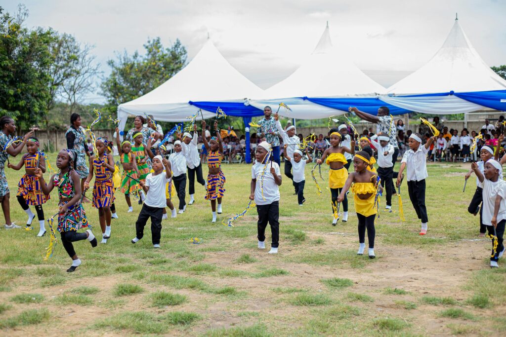 Children in traditional attire performing a lively dance at an outdoor event in Winneba, Ghana.