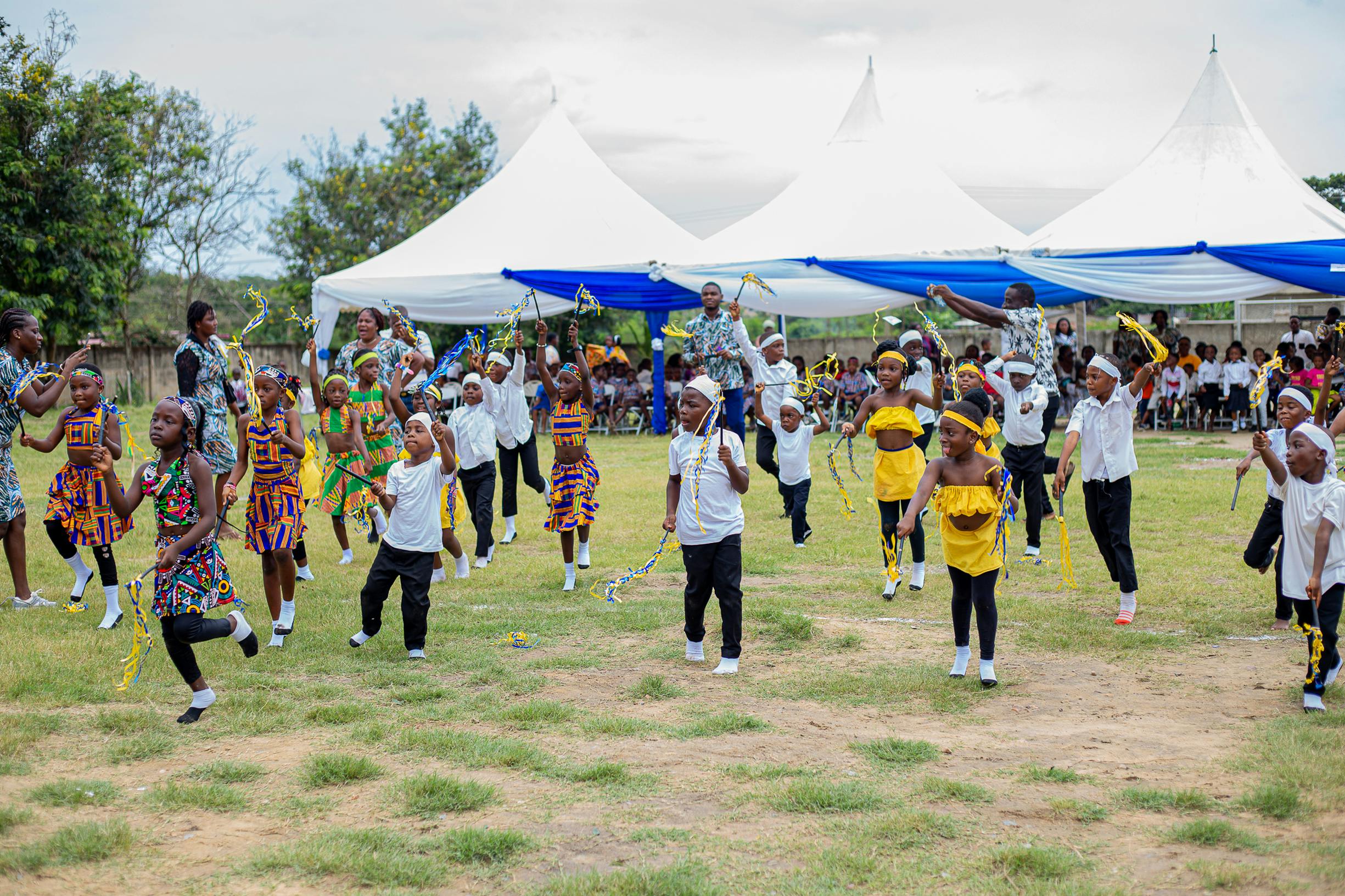 Children in traditional attire performing a lively dance at an outdoor event in Winneba, Ghana.