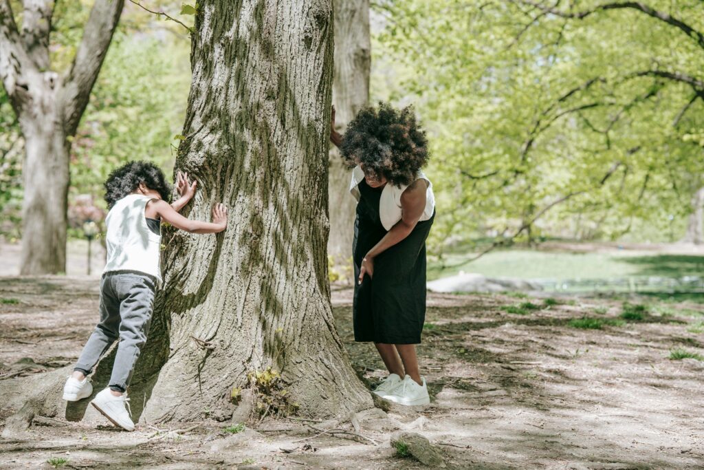 A joyful moment of a mother and child playing hide and seek around a tree in a park.